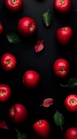 Fresh red apples and scattered green and burgundy leaves arranged on dark background, creating dramatic contrast for food photography and healthy lifestyle concepts.