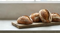 Freshly baked artisan bread loaves with crispy crusts arranged on rustic wooden cutting board in modern kitchen setting for bakery and food photography.
