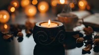 Cozy autumn evening scene with burning candle in decorative holder surrounded by coffee beans and warm bokeh lights creating peaceful ambiance for relaxation.