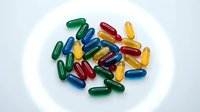 Colorful vitamin capsules and pills scattered on white plate for health supplement and nutrition concepts.