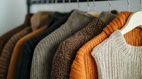 Cozy knitted sweaters in autumn colors hanging on wooden hangers. Warm wardrobe collection featuring brown, orange, and beige woolen garments arranged in row.