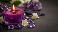 Purple candle burning surrounded by amethyst crystals, lavender flowers and jasmine blossoms creating peaceful spa atmosphere for relaxation and meditation.