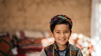 Young boy with dark hair and warm smile wearing traditional patterned vest and striped shirt, portrait photography for cultural representation and diversity themes.