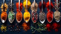 Colorful spices and herbs in silver spoons on dark background, overhead view of aromatic seasonings including turmeric, paprika, peppercorns and rosemary.