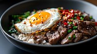 Korean beef bulgogi bowl with fried egg, rice, vegetables and sesame seeds served in ceramic dish for Asian cuisine menu and restaurant promotion.
