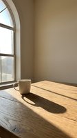 Ceramic mug on wooden table by arched window with natural sunlight casting shadows, minimalist workspace for coffee break, morning routine, or creative work environment.