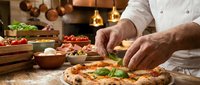 Professional chef adding fresh basil to homemade pizza in restaurant kitchen with copper pots and fresh ingredients creating authentic Italian cuisine.