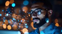 Young African American man with beard and glasses smiling while illuminated by glowing bokeh lights creating magical evening atmosphere. Blue and orange color scheme.