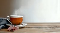 Steaming cup of hot tea on rustic wooden table with delicate pink flowers, cozy morning atmosphere with soft natural lighting and copy space.