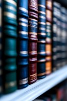 Row of vintage leather-bound books on wooden shelf, focusing on burgundy and blue spines with shallow depth of field creating atmospheric library backdrop.