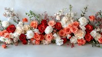 Fresh floral arrangement with red, coral, and white roses adorned with delicate greenery and small blossoms creates romantic wedding decoration on light background.