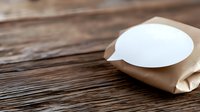 Minimalist composition of blank white speech bubble on kraft paper against rustic wooden background, symbolizing communication and messaging concepts.