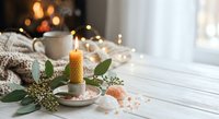 Cozy winter morning scene with burning candle, eucalyptus branches, warm coffee mug and soft knitted blanket creating peaceful hygge atmosphere indoors.