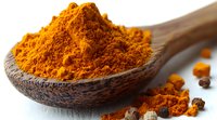 Ground turmeric powder in wooden spoon with scattered spices on white surface, bright orange color and aromatic seasoning for cooking and natural medicine.