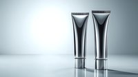 Metallic cosmetic tubes on light background with reflective surface and soft shadows. Minimalist product photography for beauty and skincare advertising.
