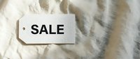 White sale tag with bold black text on soft linen fabric background, retail discount concept for fashion and shopping promotions.