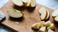 Fresh apple slices on wooden cutting board ready for healthy snacking, cooking or baking preparation in bright kitchen setting.