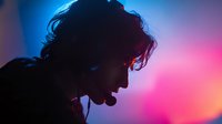 Silhouette of person with curly hair against vibrant blue and pink gradient background, creating dramatic profile in nightclub atmosphere.