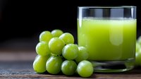 Fresh green grape juice in glass with ripe juicy grapes cluster on dark wooden background, healthy natural beverage for detox and wellness.