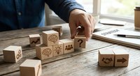 Business professional arranging wooden blocks with innovation symbols including lightbulb, brain, gears and question mark on office desk for strategic planning.