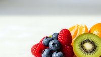 Fresh mixed berries and sliced kiwi fruit arranged on white background. Healthy organic food ingredients for smoothies, desserts and breakfast meals.