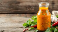 Fresh homemade spicy sauce in glass bottle with chili peppers, garlic and herbs on rustic wooden background. Natural condiment for cooking.