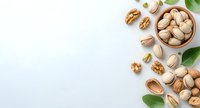Mixed nuts scattered on light blue background with green leaves. Pistachios in wooden bowl and walnuts create natural border composition for healthy food design.