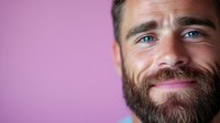 Smiling bearded Caucasian man with bright eyes against purple background, cropped portrait showing genuine happiness and confidence. Professional headshot style.