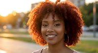 Young African American woman with curly afro hair smiling outdoors during golden hour sunset light for lifestyle and beauty content.