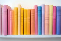 Row of colorful hardcover books arranged on white shelf, spines showing in pastel pink, yellow, orange, blue and purple tones creating rainbow effect.