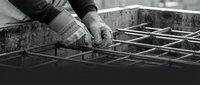 Worker in work gloves tying steel reinforcement bars together on construction site, black and white industrial photography for building and construction projects.