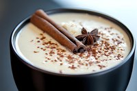 Creamy chai latte topped with cinnamon sticks, star anise and cocoa powder in black ceramic cup, macro shot with selective focus on spices and foam.