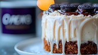 Decadent cheesecake topped with chocolate sandwich cookies and white chocolate drips on chocolate cookie base, served on white plate. Close-up food photography.
