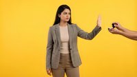 Young Hispanic businesswoman in beige suit making stop gesture refusing alcohol on yellow background. Professional woman saying no to drinking habits.