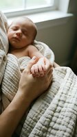 Peaceful newborn baby sleeping while holding parent finger in soft natural light by window creating tender bonding moment for family photography.
