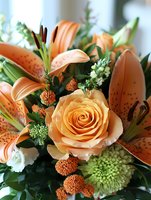 Fresh floral arrangement featuring peach roses, orange spotted lilies, green chrysanthemums and small white blooms against dark green foliage in natural lighting.