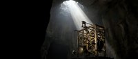 Sunlight streams through cave opening onto ornate wooden structure in dark cavern, creating dramatic atmospheric lighting for exploration and adventure themes.