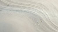 Smooth sand texture with natural wind-carved patterns and gentle curves creating organic flowing lines across beach surface for backgrounds and textures.