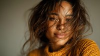Young Hispanic woman with tousled hair in warm golden light wearing cozy knit sweater with natural makeup and gentle smile for lifestyle photography.