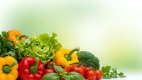 Fresh organic vegetables including bell peppers, tomatoes, broccoli and leafy greens arranged on soft green background for healthy eating and nutrition concepts.
