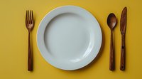 Empty white ceramic plate with wooden cutlery set including fork, knife and spoon arranged on vibrant yellow background, minimalist table setting composition.
