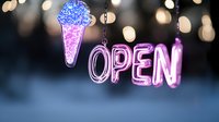 Glowing neon pink open sign with ice cream cone illuminated against blurred bokeh lights background creates welcoming atmosphere for food service business.