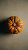 Orange pumpkin with natural ridges and stem on neutral beige background for autumn harvest decorations and seasonal cooking projects.