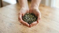 Caucasian male hands holding a handful of raw sunflower seeds over a wooden surface, representing healthy snacking, nutrition, and organic food selection for culinary use.