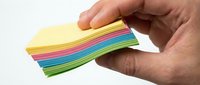 Person holding stack of colorful sticky notes fanned out, displaying rainbow colors including yellow, pink, blue, and green for organization and planning needs.