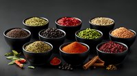 Colorful spices and seasonings in black ceramic bowls on dark background with scattered ingredients. Traditional cooking condiments collection for culinary design.