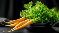 Fresh organic carrots with green leaves and black ceramic bowl on dark background, healthy raw vegetables for cooking and salads.