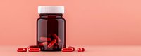 Red capsules and dark brown medicine bottle on pink background, minimalist pharmaceutical composition for healthcare and supplement marketing.