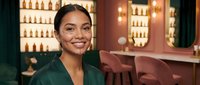 Young Hispanic woman smiling in upscale bar restaurant with warm lighting and bottles display background for hospitality service industry concepts.