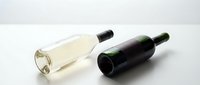 Two wine bottles lying on white surface, one clear glass with white wine and one dark green bottle, minimalist product photography for beverage industry marketing.